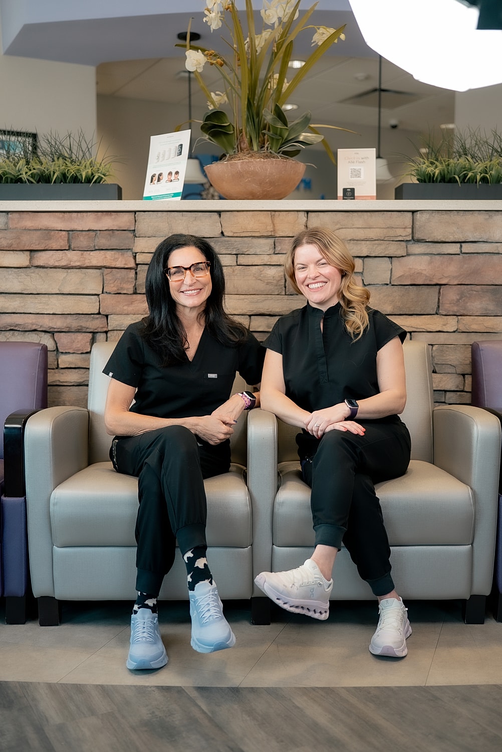Two women sitting in medical scrubs, smiling.