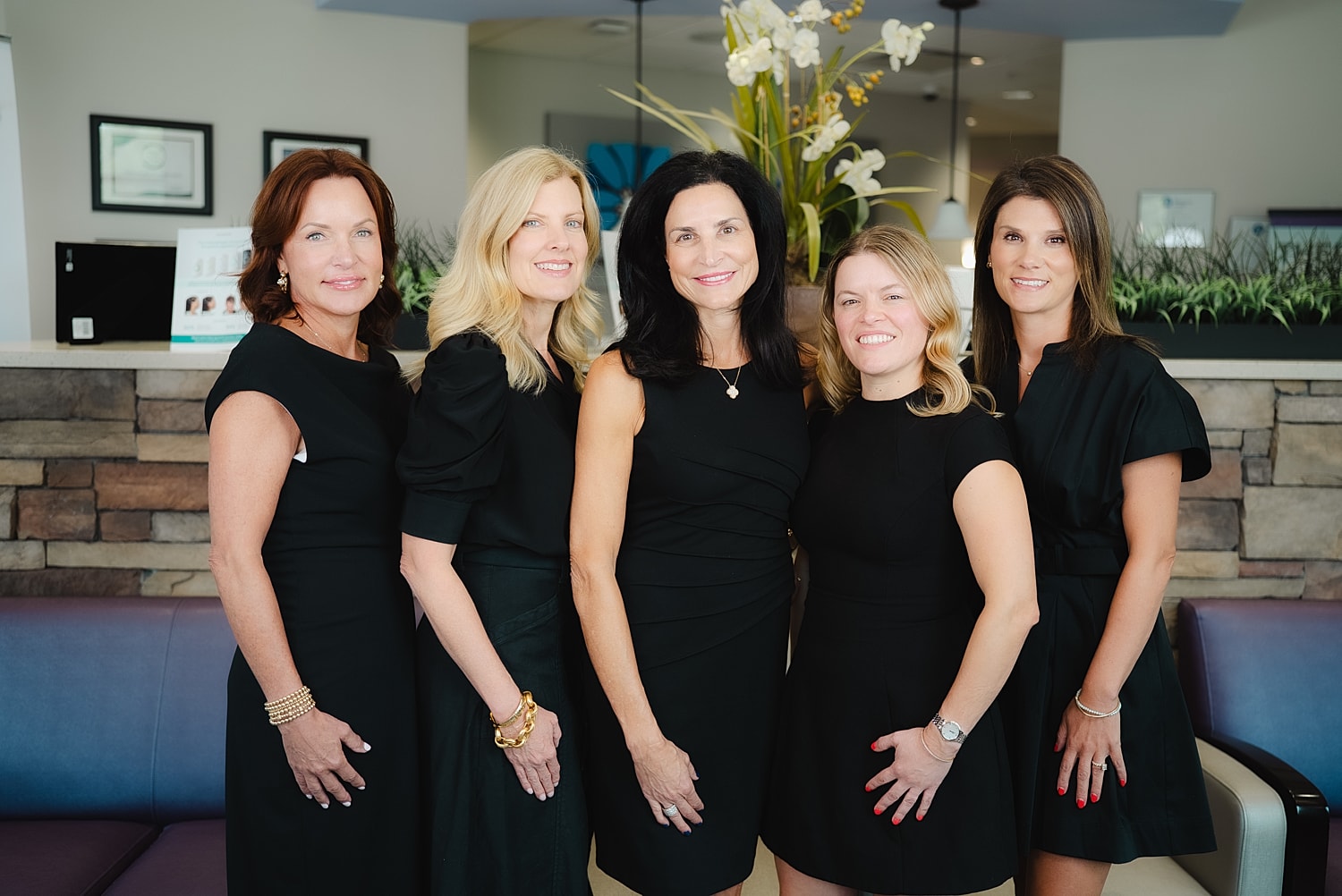 Five women in black dresses posing together.