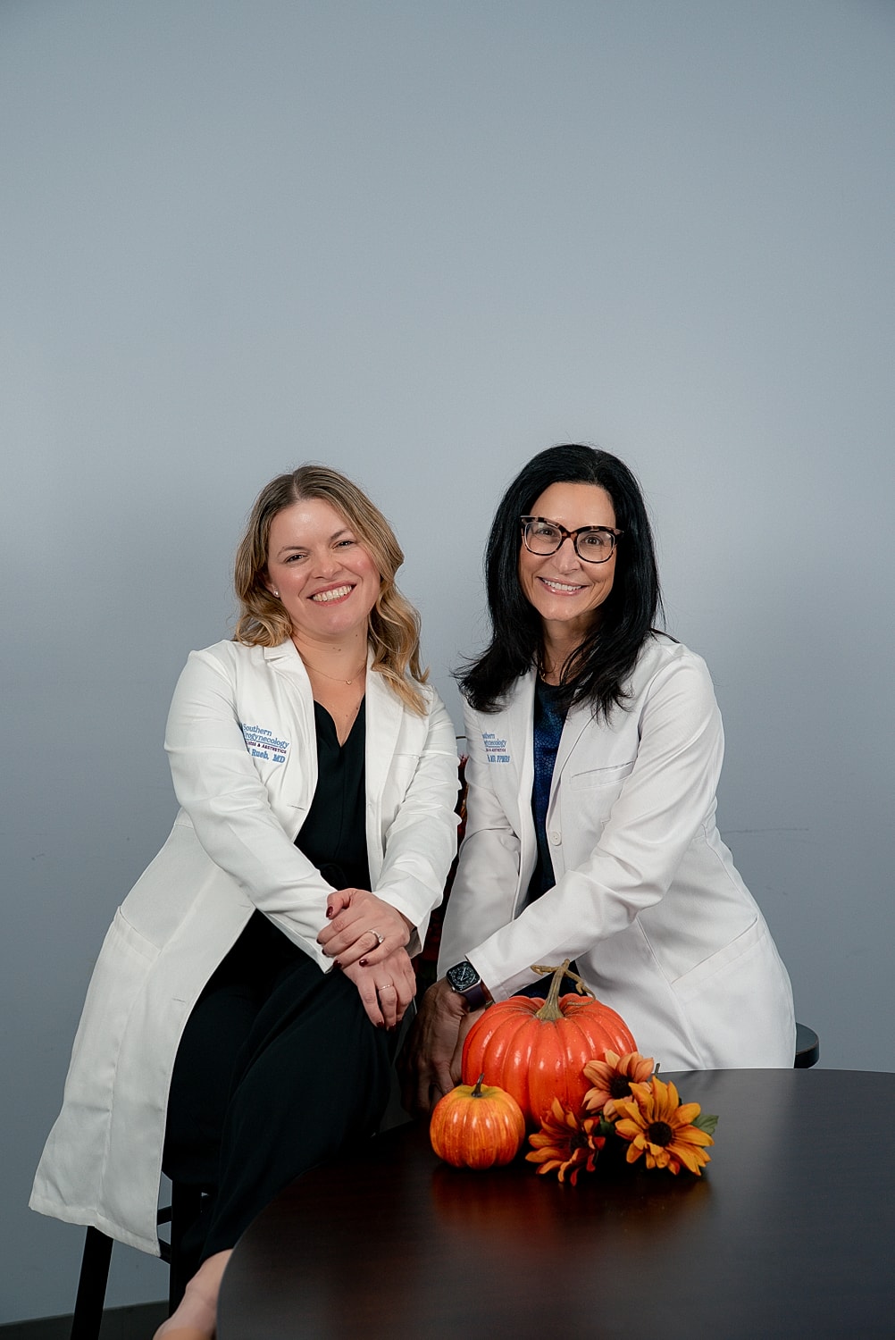 Two women in lab coats with pumpkins.