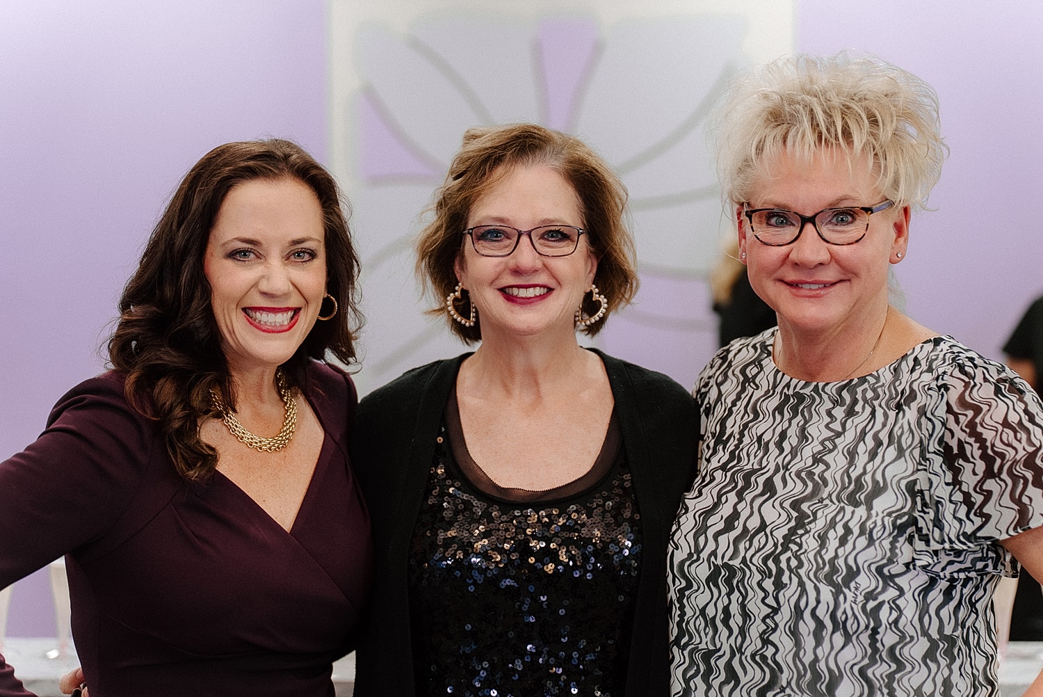Three smiling women posing together indoors.