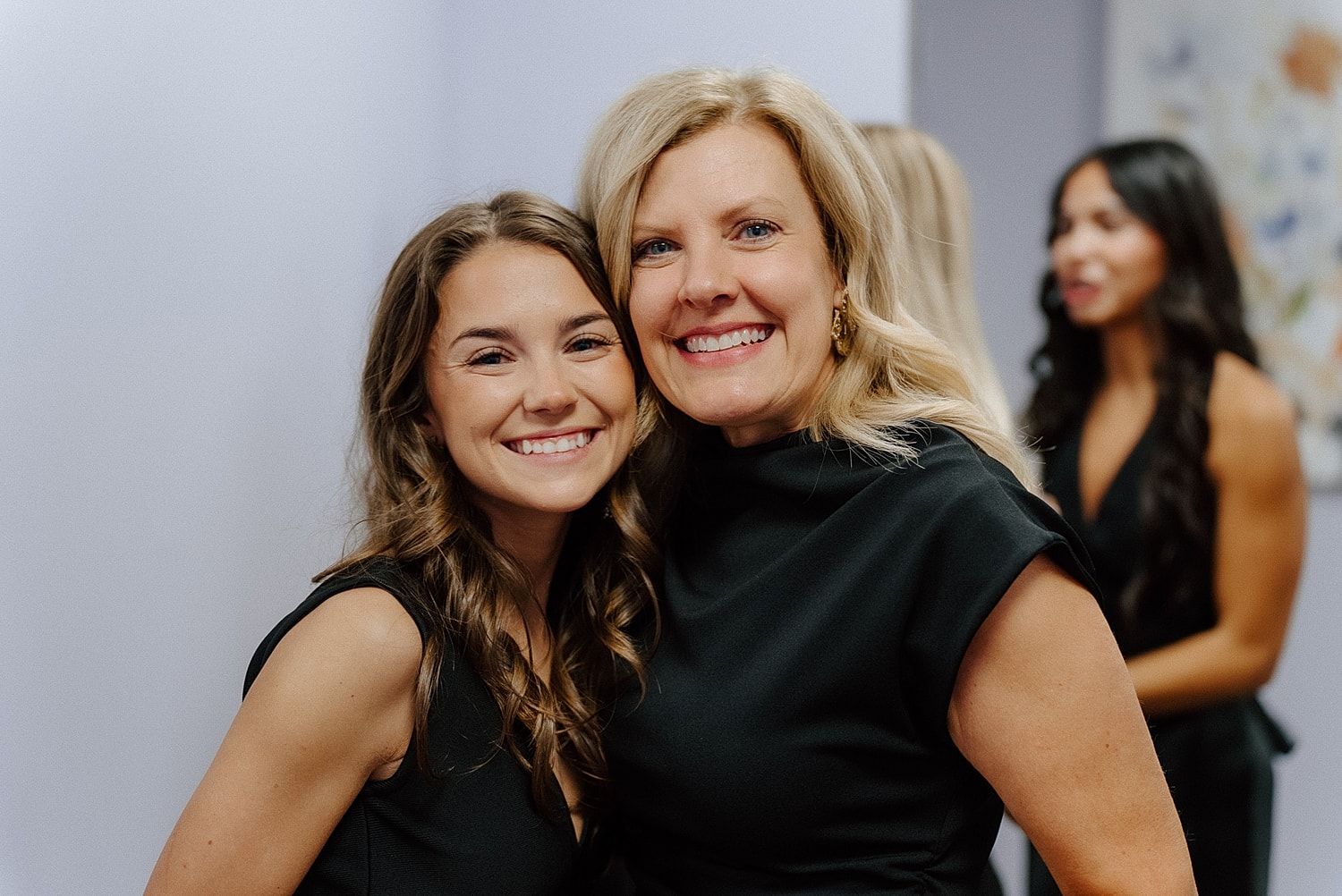 Two women smiling together in black dresses.