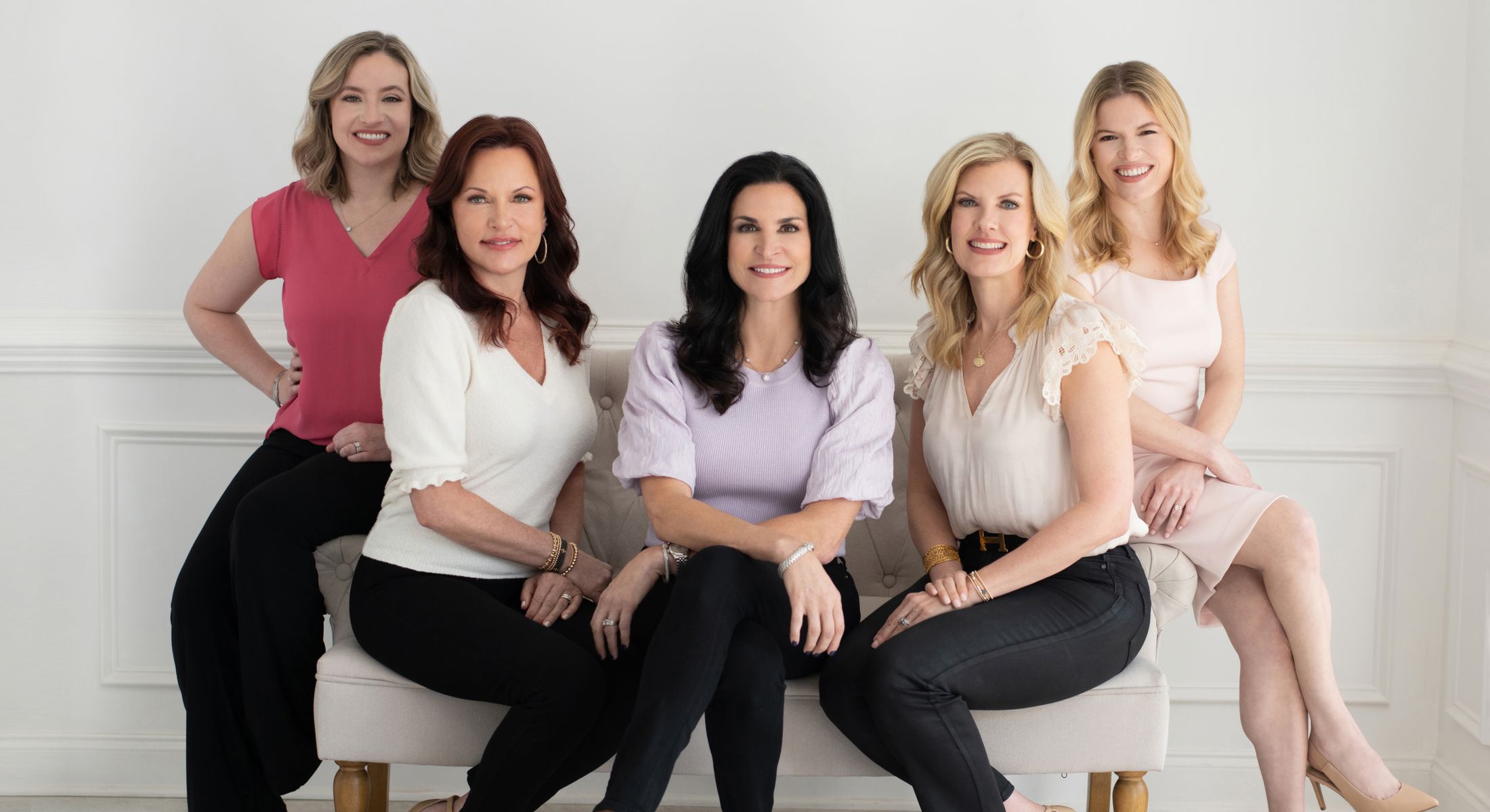 Five women posing together in a bright setting.